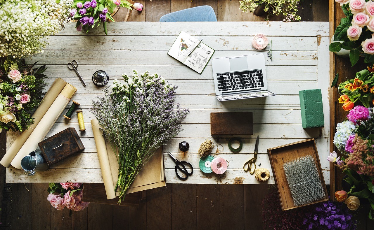assorted flowers and office items (computer, scissors, twine, etc) on a wooden table