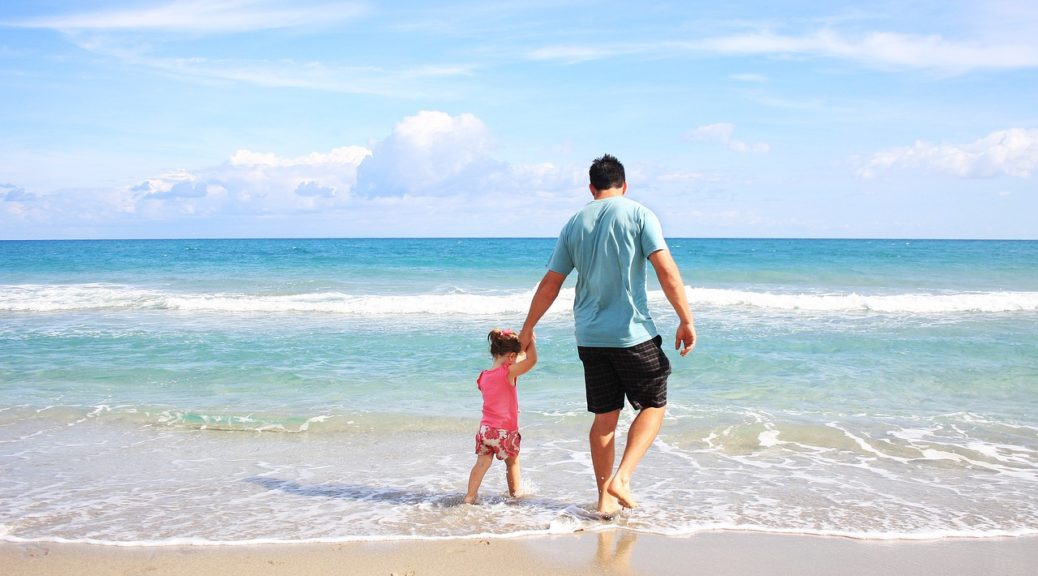 a man holding a child's hand, stepping into the ocean surf