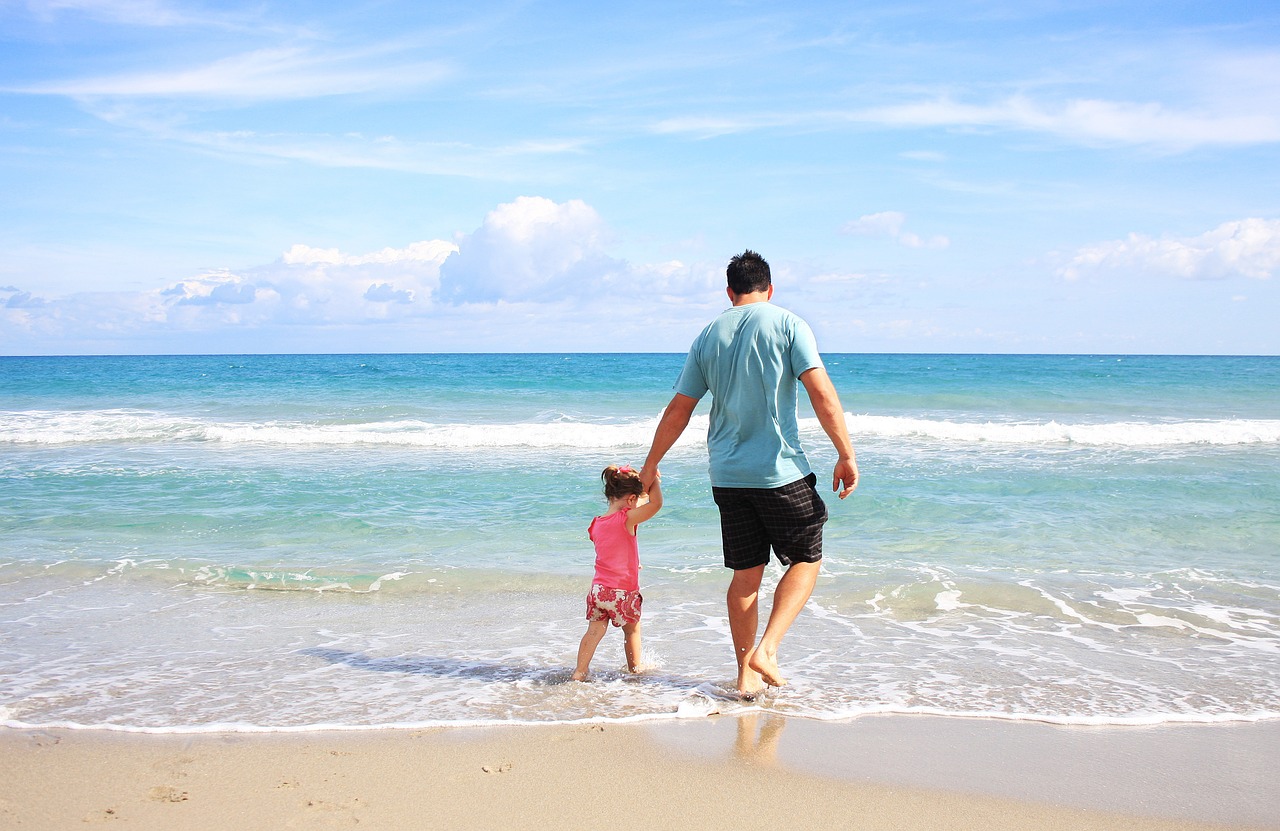 a man holding a child's hand, stepping into the ocean surf