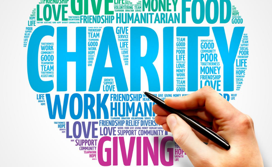 a hand holding a pen in front of a heart illustration filled with words including "charity," "work," "giving," and "life."